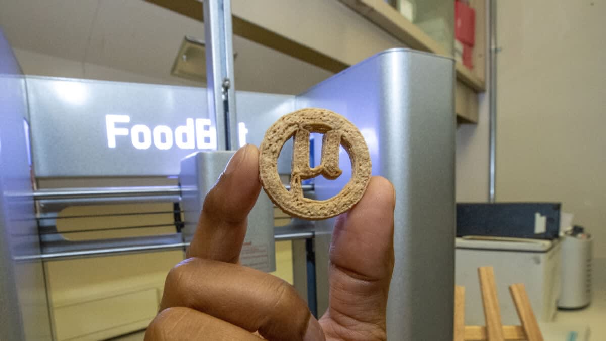 Researcher holding cookie-shaped food made from recycled plastic bottles in laboratory setting