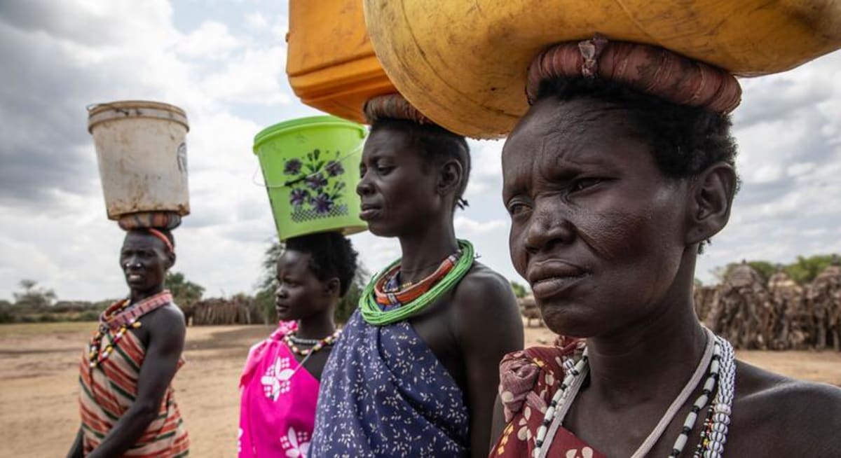 ** Women walking across dry landscape in South Sudan carrying water containers on their heads