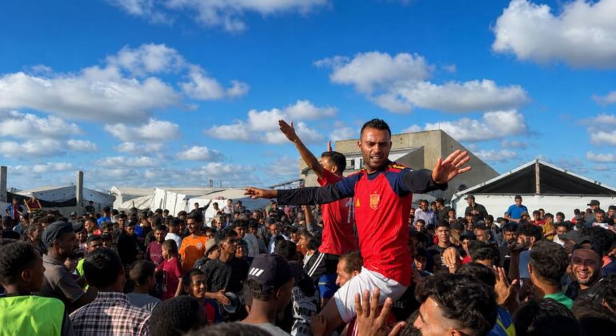 Football players celebrate on sandy pitch surrounded by displacement camp tents in Gaza