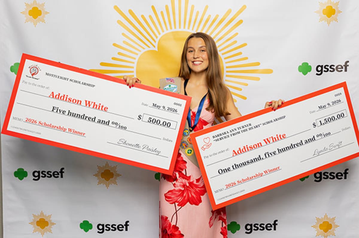 Girl Scout Addison White holding two scholarship award certificates while wearing Girl Scout uniform