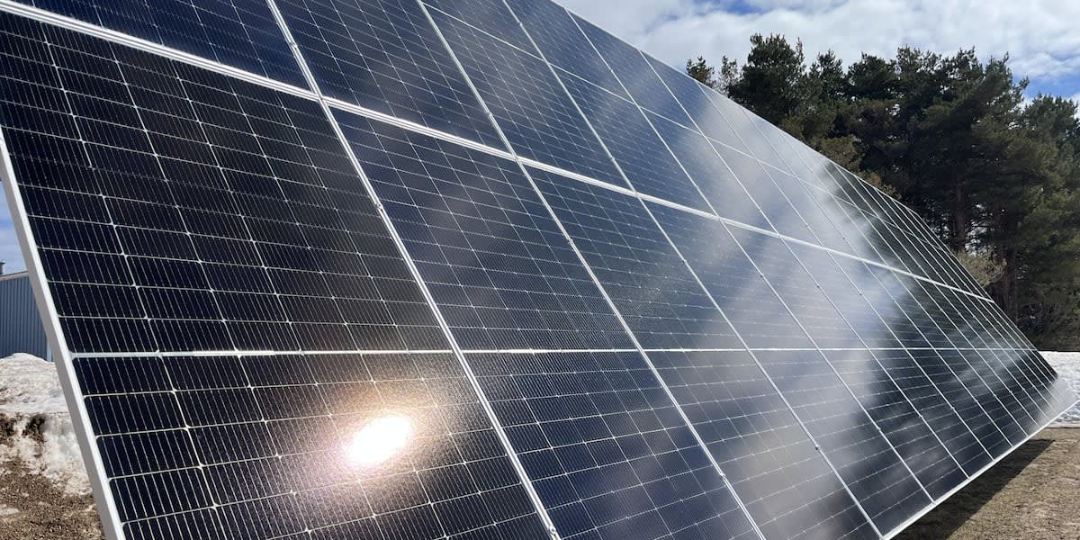 Workers installing metal roofing with integrated solar panels at manufacturing facility