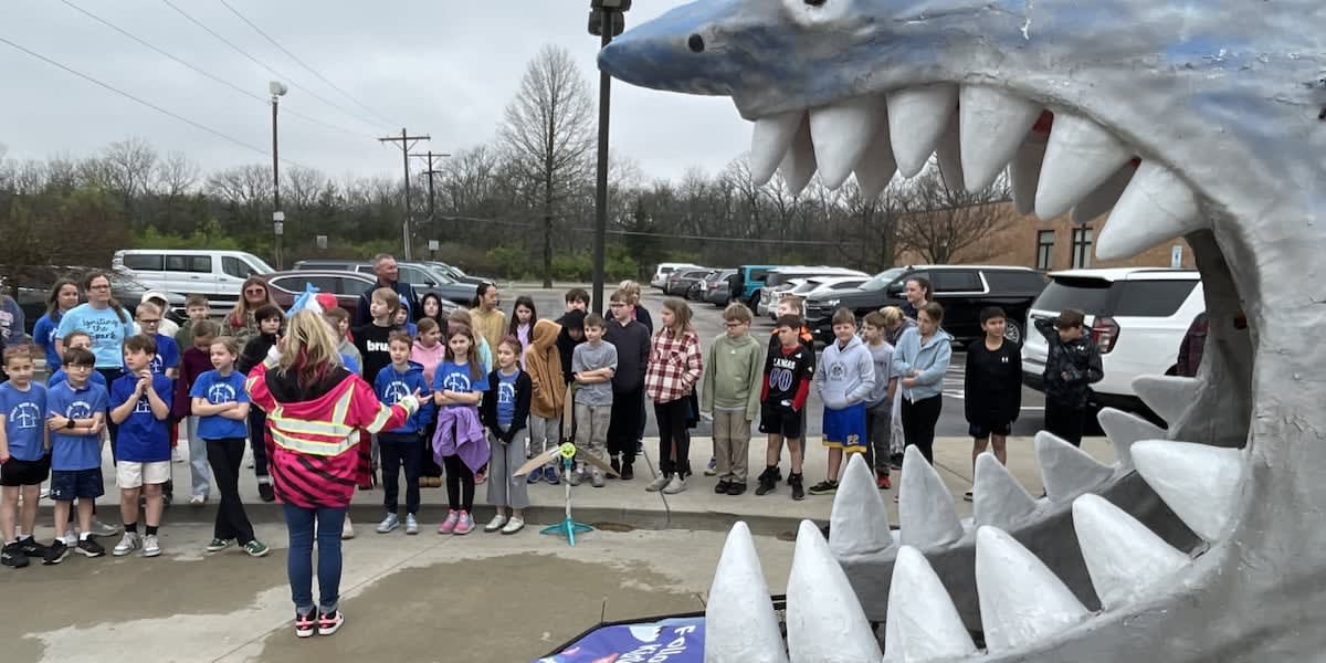 Elementary students watching their wind turbine designs spin in a large shark-shaped wind tunnel