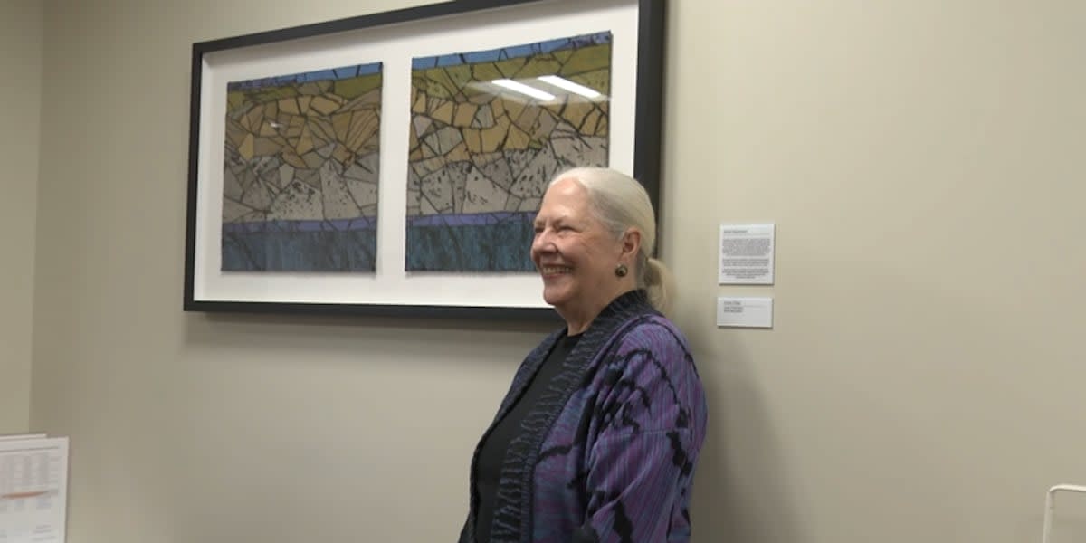 Artist Chris Triola stands beside her colorful textile art piece hanging in cancer center