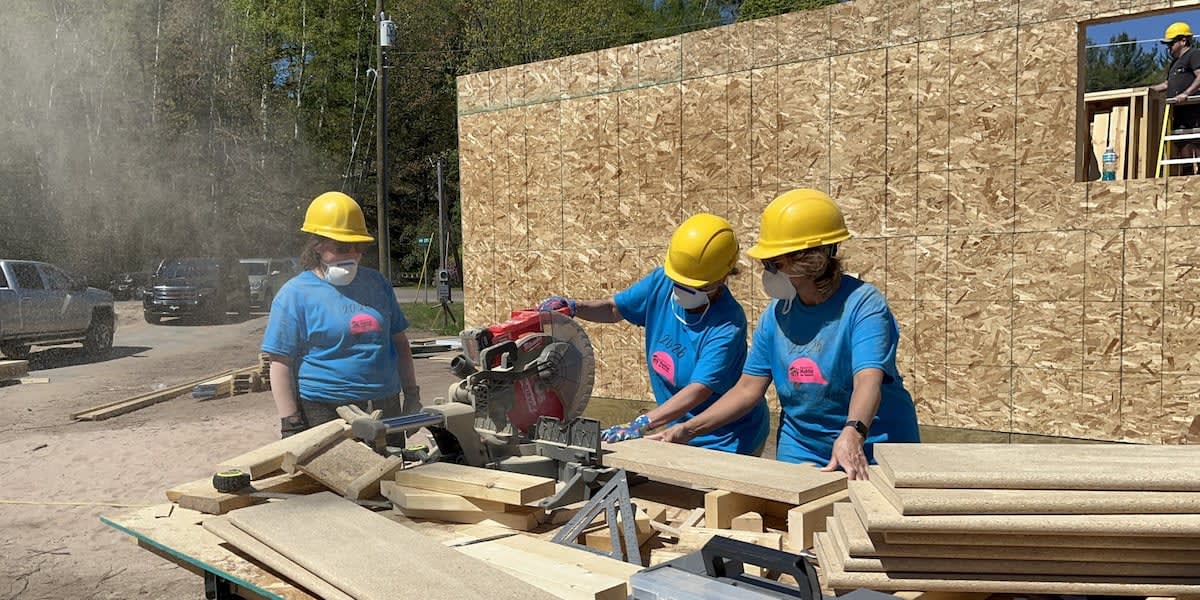 Women volunteers in hard hats constructing wooden house frame at Habitat for Humanity build site