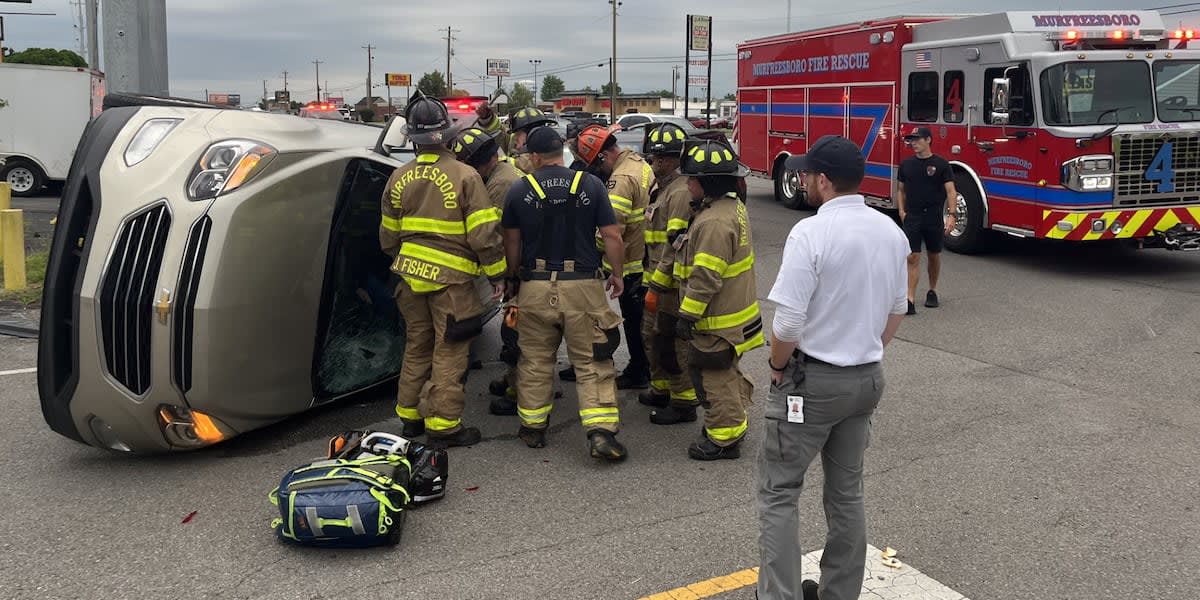 Tan Chevy sedan overturned on its side at Murfreesboro intersection with emergency vehicles nearby