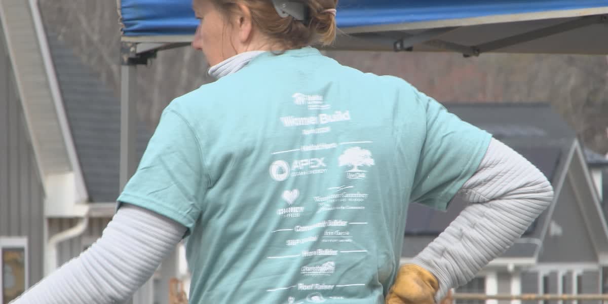 Female volunteers in hard hats building wooden frame walls at Habitat for Humanity construction site