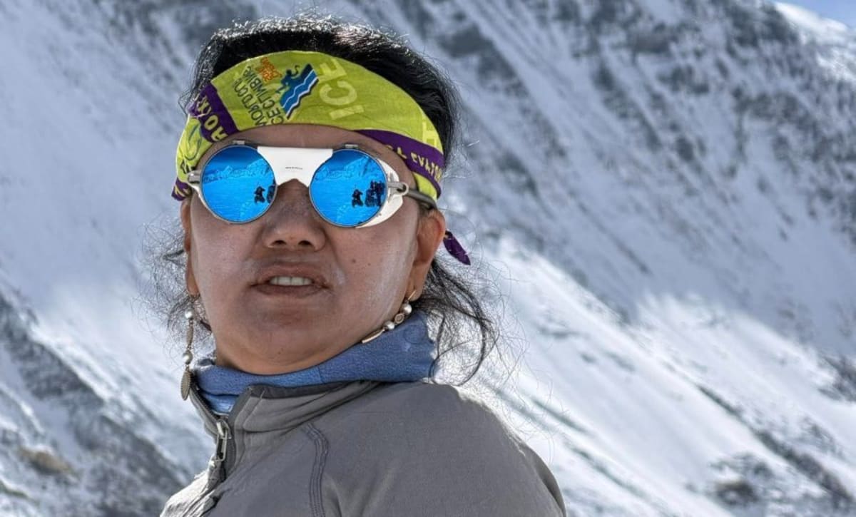 Lhakpa Sherpa in climbing gear on a snowy mountain peak holding climbing equipment