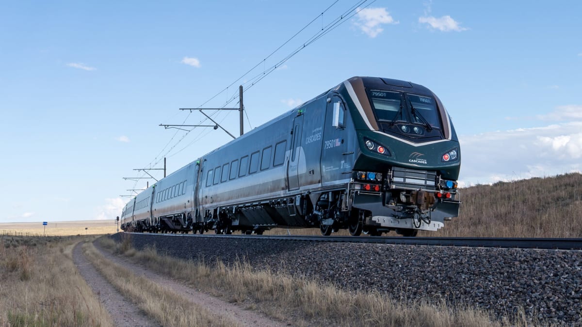 Modern silver Amtrak Airo train traveling through scenic Pacific Northwest landscape with mountains
