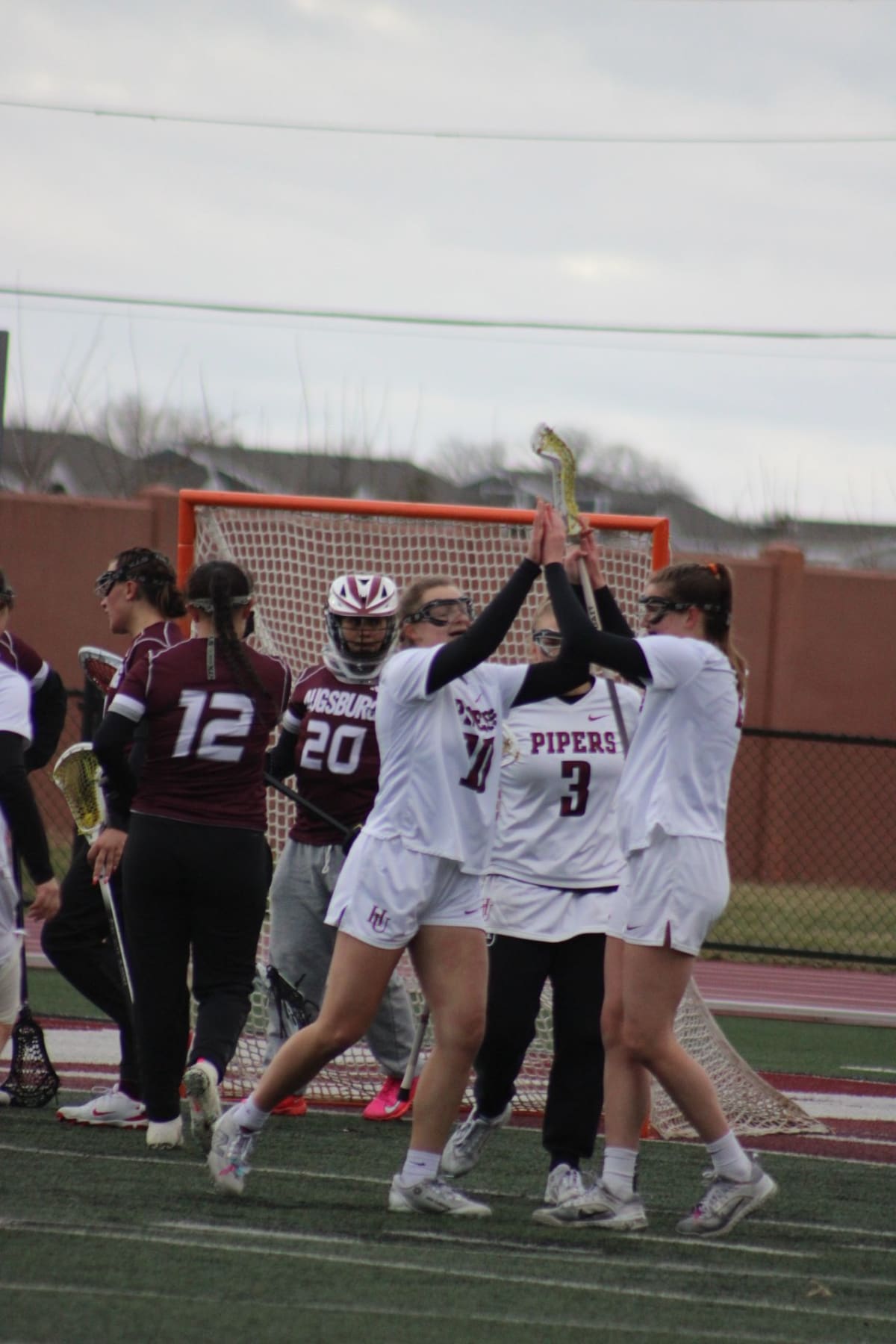 Hamline University lacrosse players Ema Rehder, Kayli Starkey and Ella Dallmann celebrating victory on field