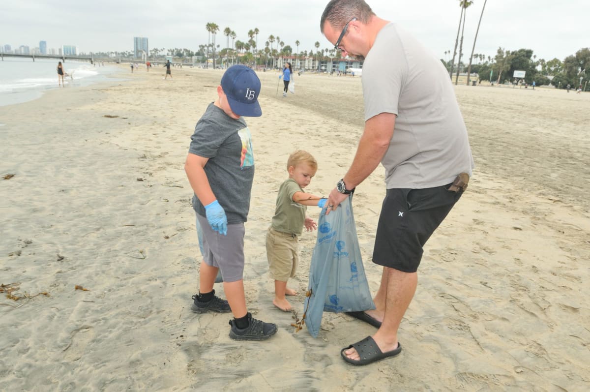 Volunteers collecting trash and debris along sunny Long Beach California coastline during community cleanup event