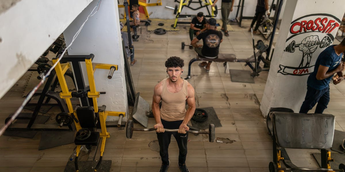 ** Men lifting weights in basement gym with sunlight through bomb-damaged walls in Gaza