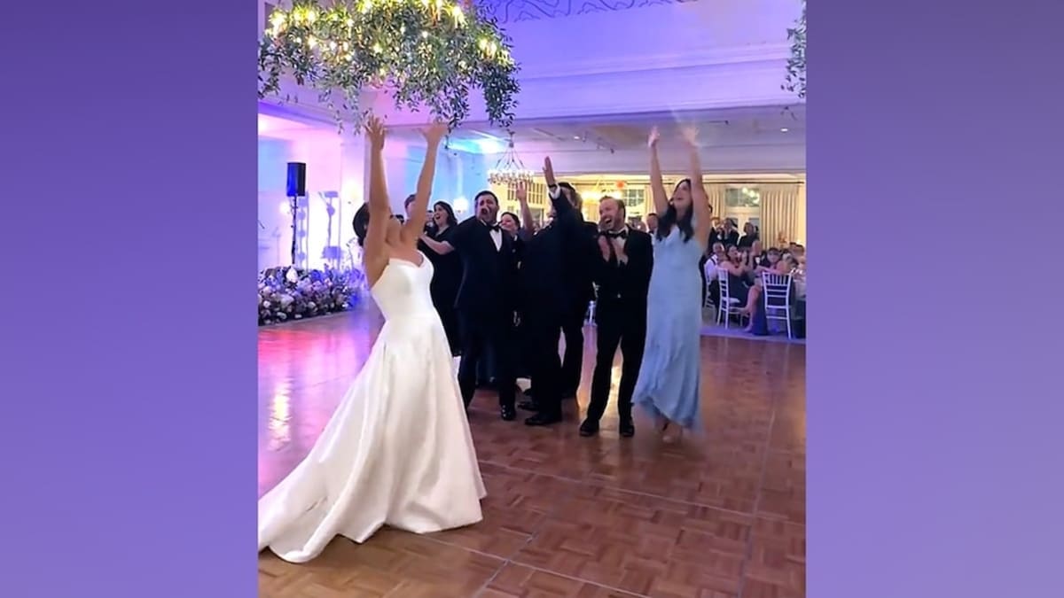 Bride in white dress reacting emotionally to surprise Broadway performance at wedding reception