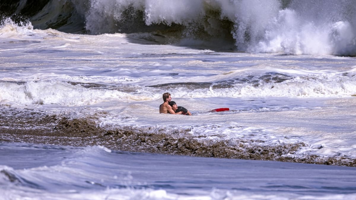 Teen lifeguard Ryder Williams pulling young boy through massive crashing waves at California beach