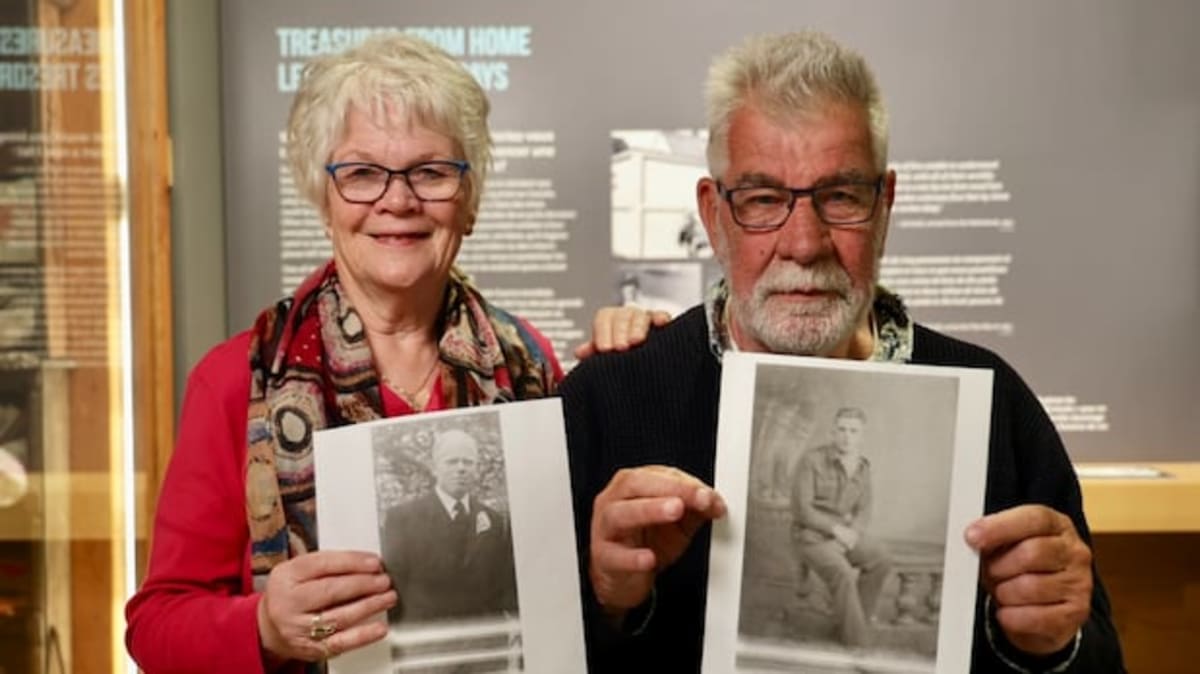 Two people holding old photographs of their fathers who met during World War II