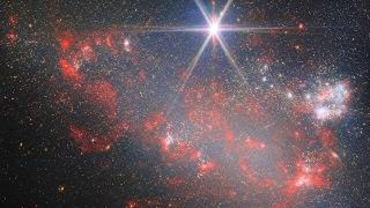 James Webb infrared image showing irregular galaxy Arp 263 with glowing blue and red star-forming regions