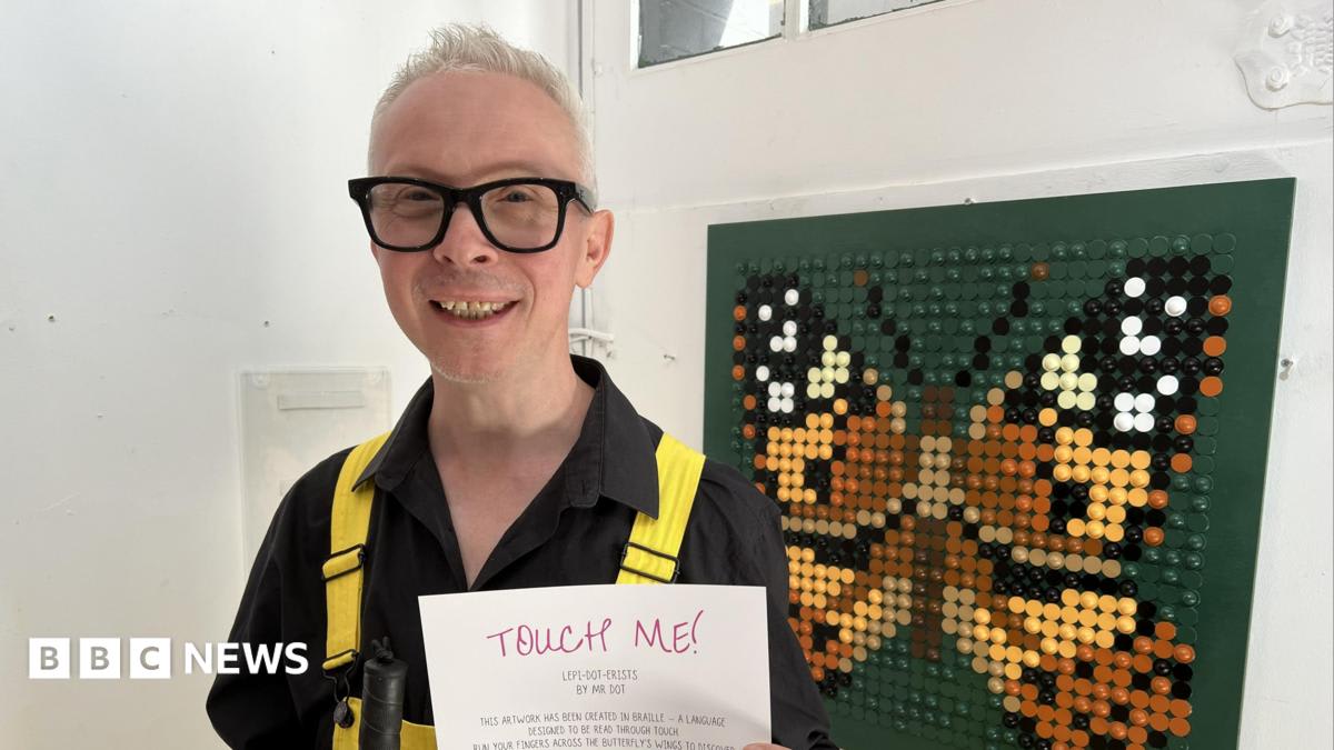 Braille artist Mr Dot standing next to colorful butterfly sculpture in Brighton street
