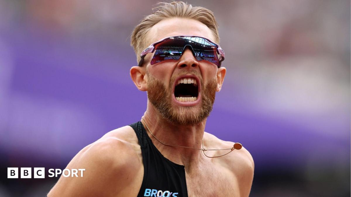 Josh Kerr celebrating with arms raised crossing finish line at packed London Stadium