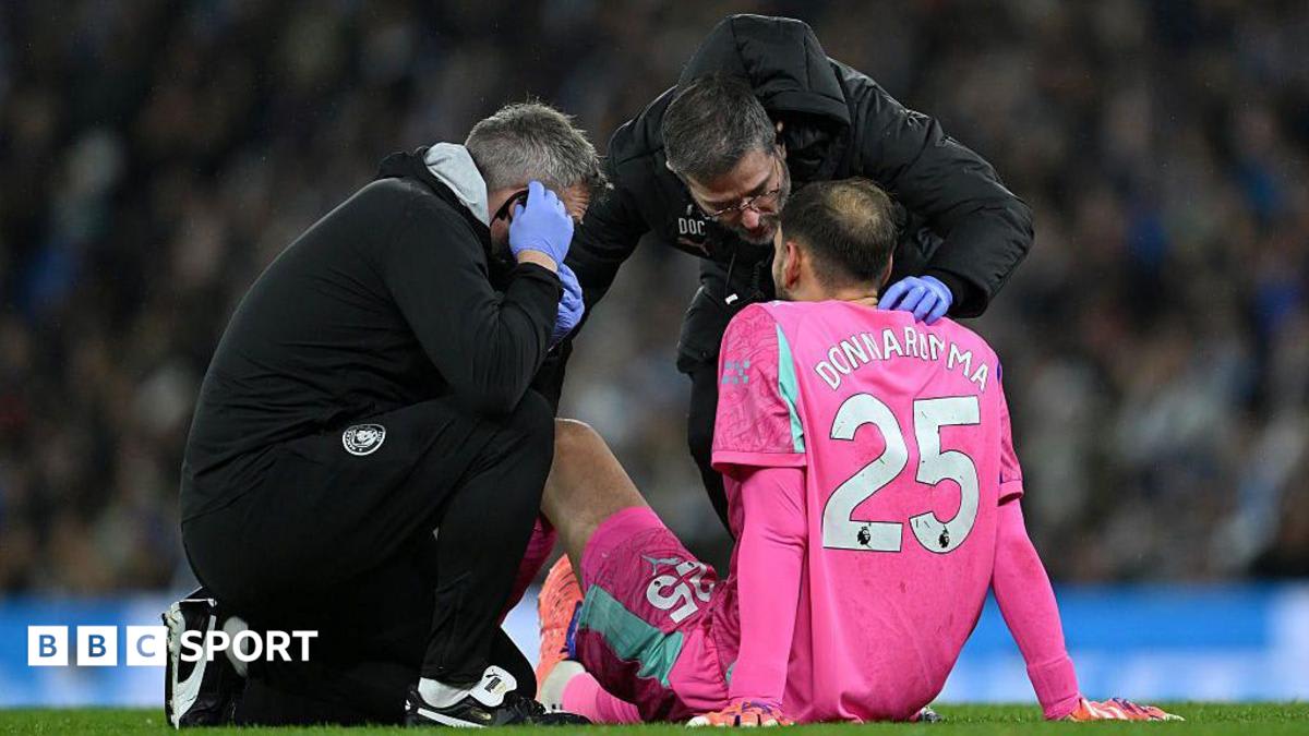 Soccer goalkeeper sitting on field receiving treatment from team physio during match stoppage