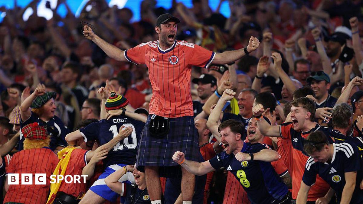 Scottish football fans in salmon pink jerseys celebrating with flags in Boston streets