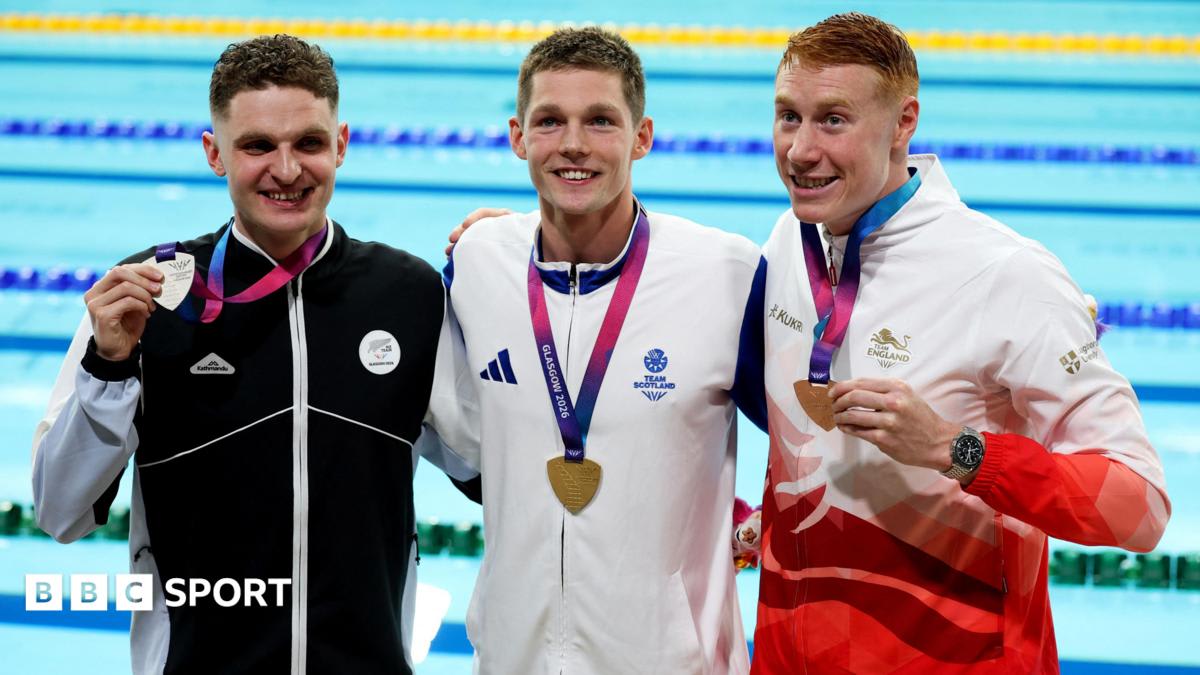 Scottish swimmer Duncan Scott celebrates on podium between New Zealand and English competitors at Glasgow pool