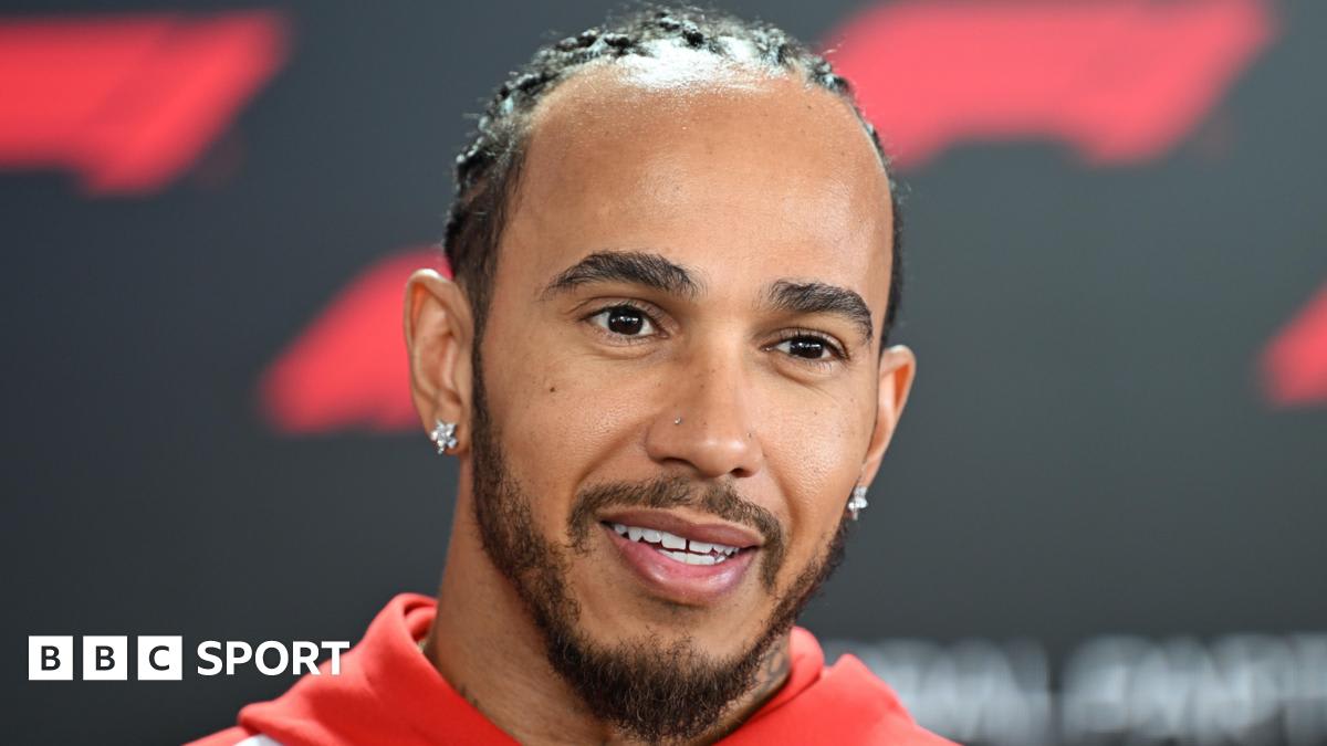 Lewis Hamilton in red Ferrari racing suit smiling at Suzuka circuit paddock