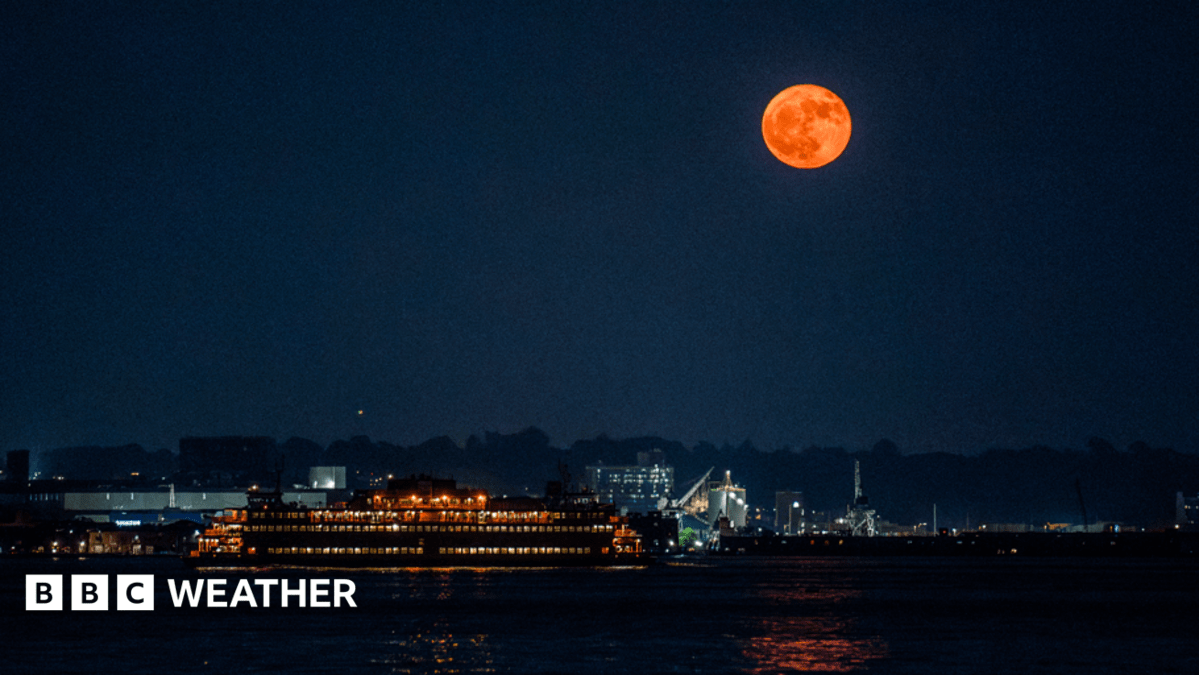 Large orange full moon sitting low on horizon above silhouetted landscape at dusk