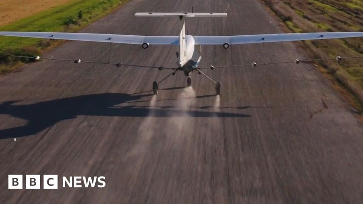 Small white autonomous electric plane flying low over green agricultural field spraying crops