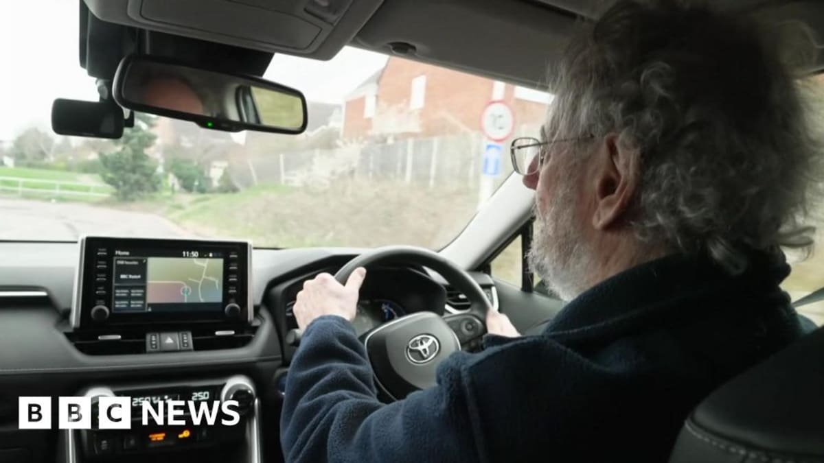 Volunteer driver Robert Turner smiling beside his car at Shrewsbury hospital entrance
