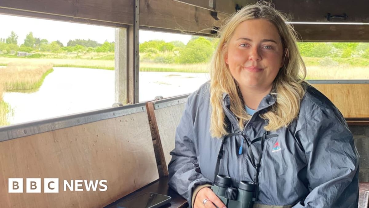 Young woman with binoculars birdwatching at coastal nature reserve on sunny day