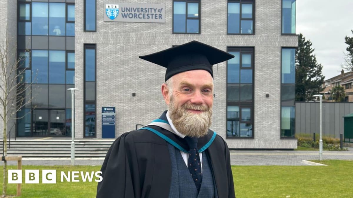 Chris Garratt holding graduation gown and mortarboard cap while wearing athletic trainers for marathon training