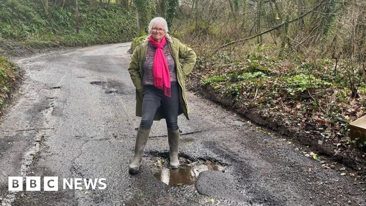 Volunteer filling pothole on rural Devon road with shovel and repair materials