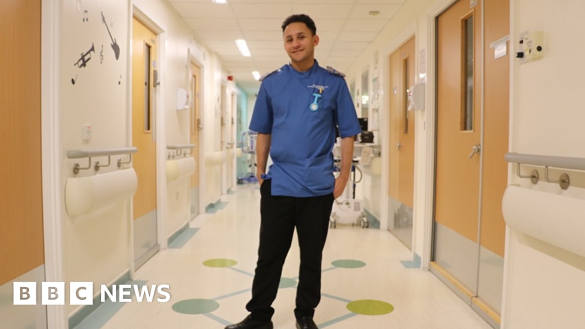 Dan Laird in nursing scrubs smiling on children's ward at University Hospitals Coventry