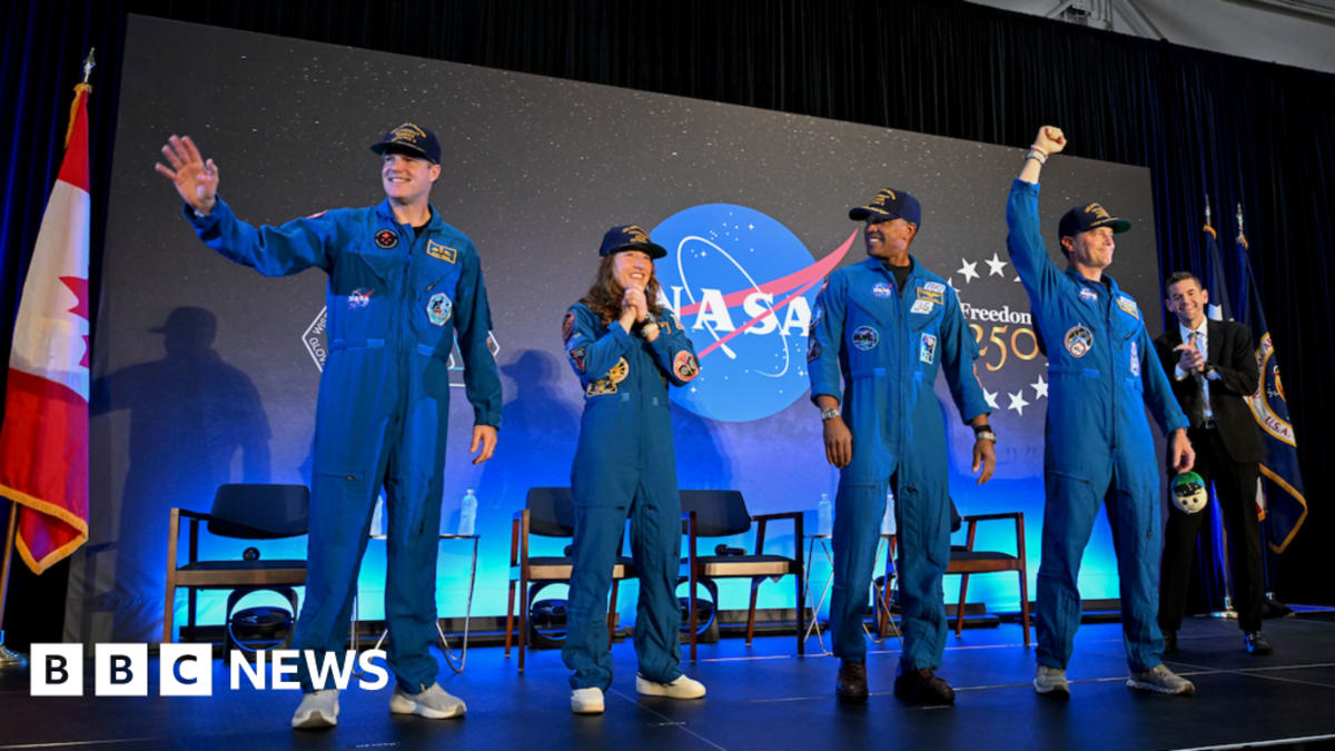 Four Artemis II astronauts in orange flight suits smiling at NASA press conference