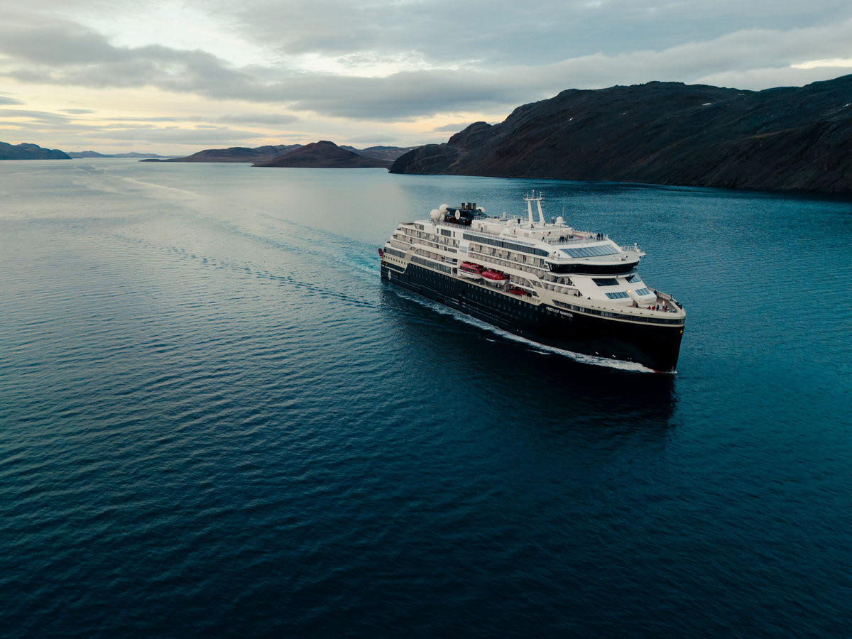 ** Expedition cruise ship sailing through pristine polar waters surrounded by ice and mountains