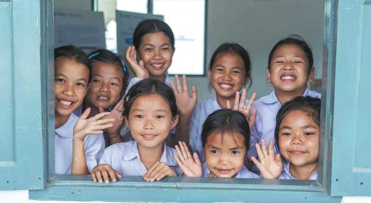 Children looking through window of small library building in rural Thinsom village, Laos