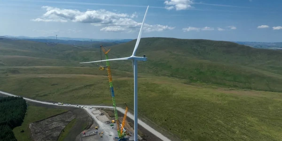 Massive white wind turbine standing tall against Scottish countryside under blue sky