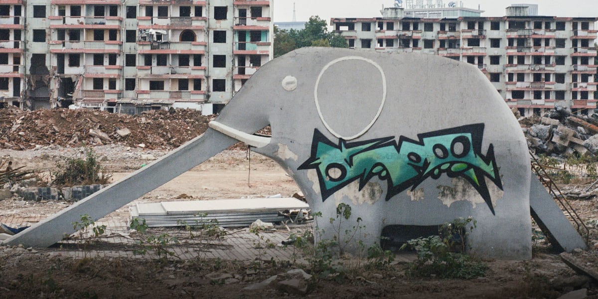 Weathered concrete elephant-shaped playground slide standing alone in abandoned park surrounded by fallen leaves