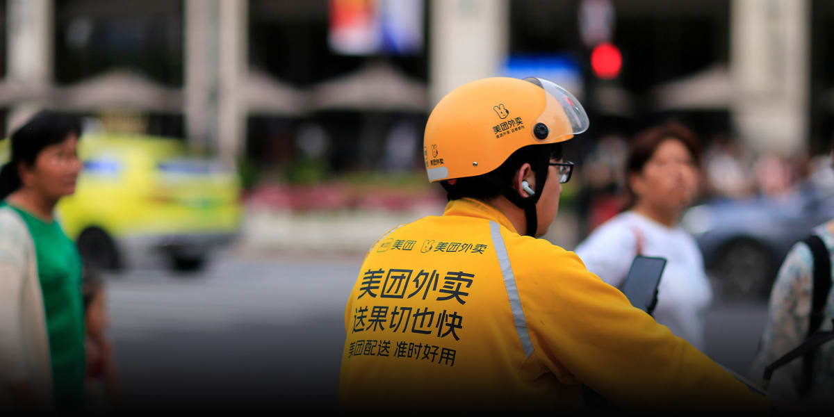 Delivery rider waiting at red traffic light while checking smartphone app in Chinese city