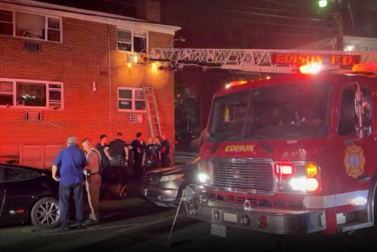Firefighters position ladder against apartment building during nighttime rescue operation in Edison