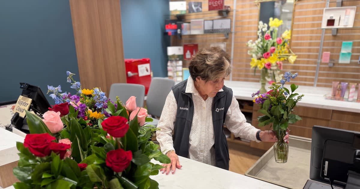 Older woman volunteer helping customer select gifts in bright hospital gift shop