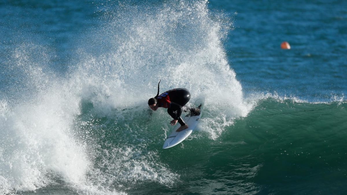 Professional surfer riding a long left-breaking wave at Raglan's Manu Bay, New Zealand