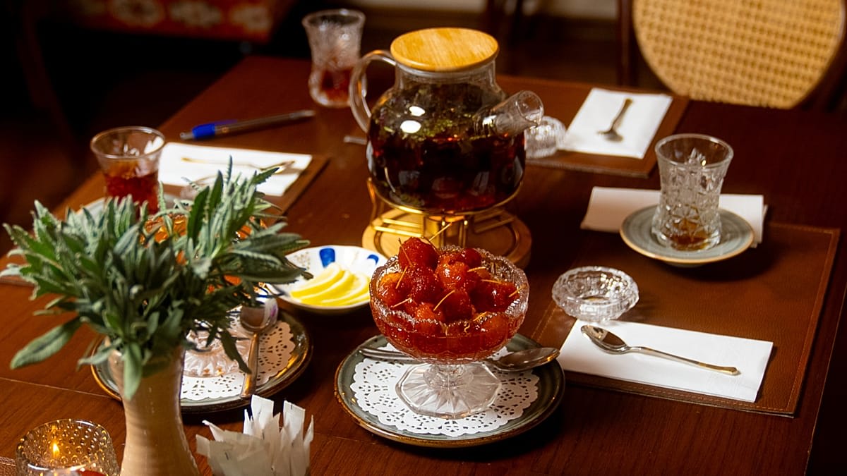 Pear-shaped Azerbaijani tea glass beside crystal bowl of handmade fruit preserves on traditional table