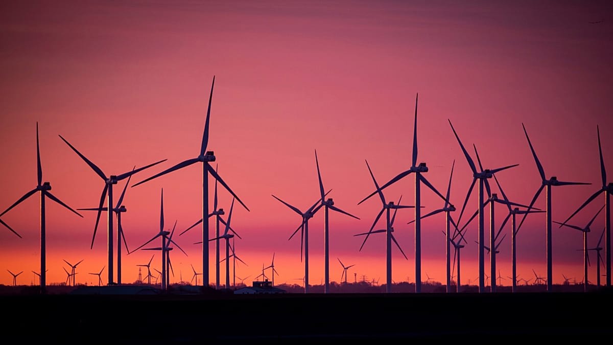 Wind turbines generating electricity against blue sky with residential homes in foreground