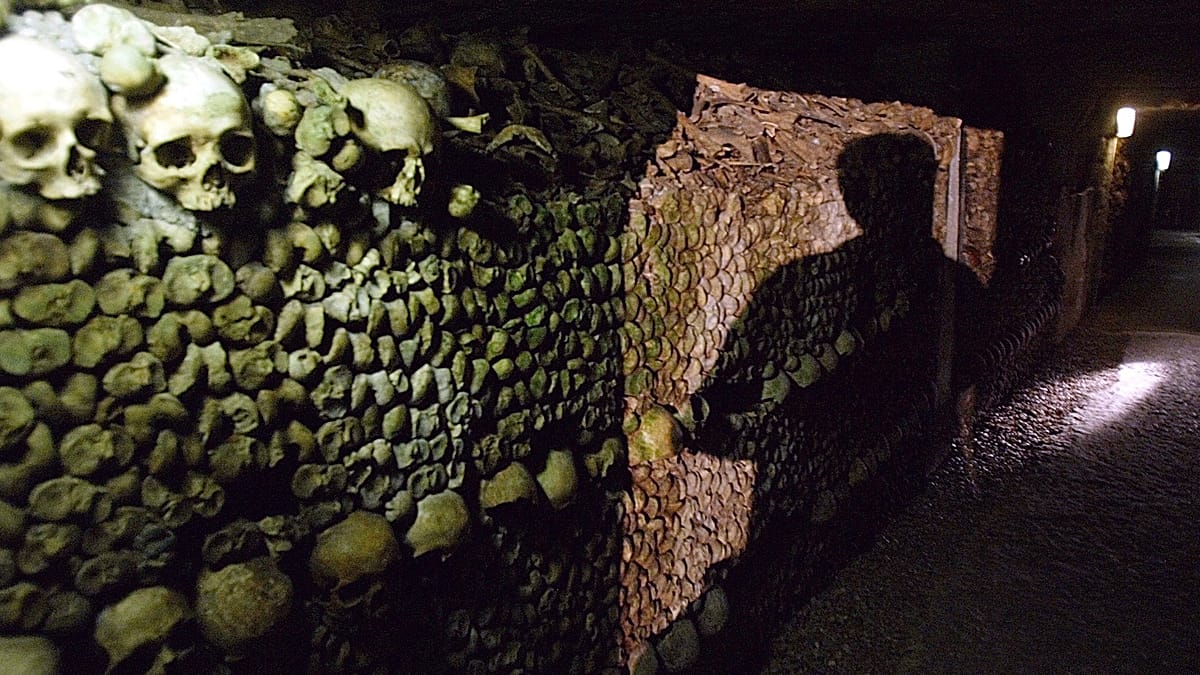 Underground tunnel in Paris Catacombs with arranged skulls and bones along stone walls