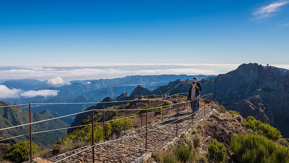 Hikers walking along mountain ridge trail above clouds on Madeira's Pico do Areeiro route