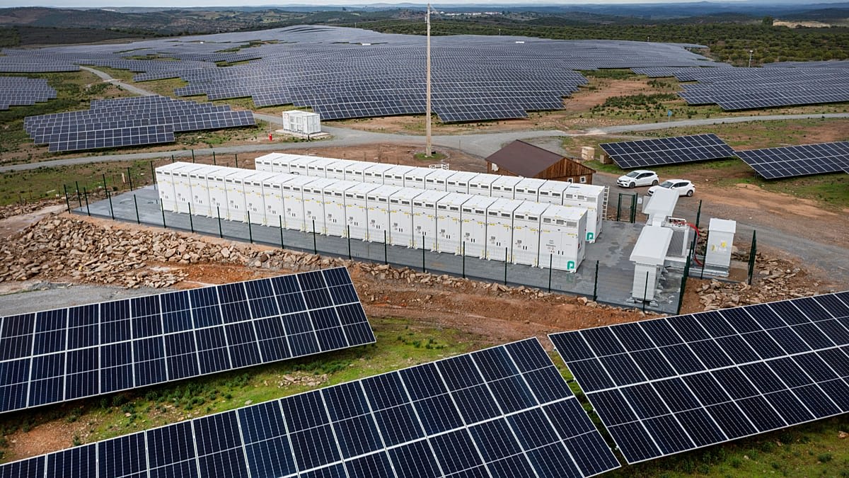 Large scale battery storage facility with solar panels in background under blue sky