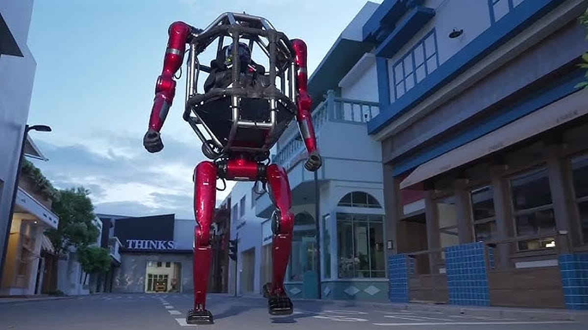Large two legged pilotable robot with open cockpit standing in industrial setting