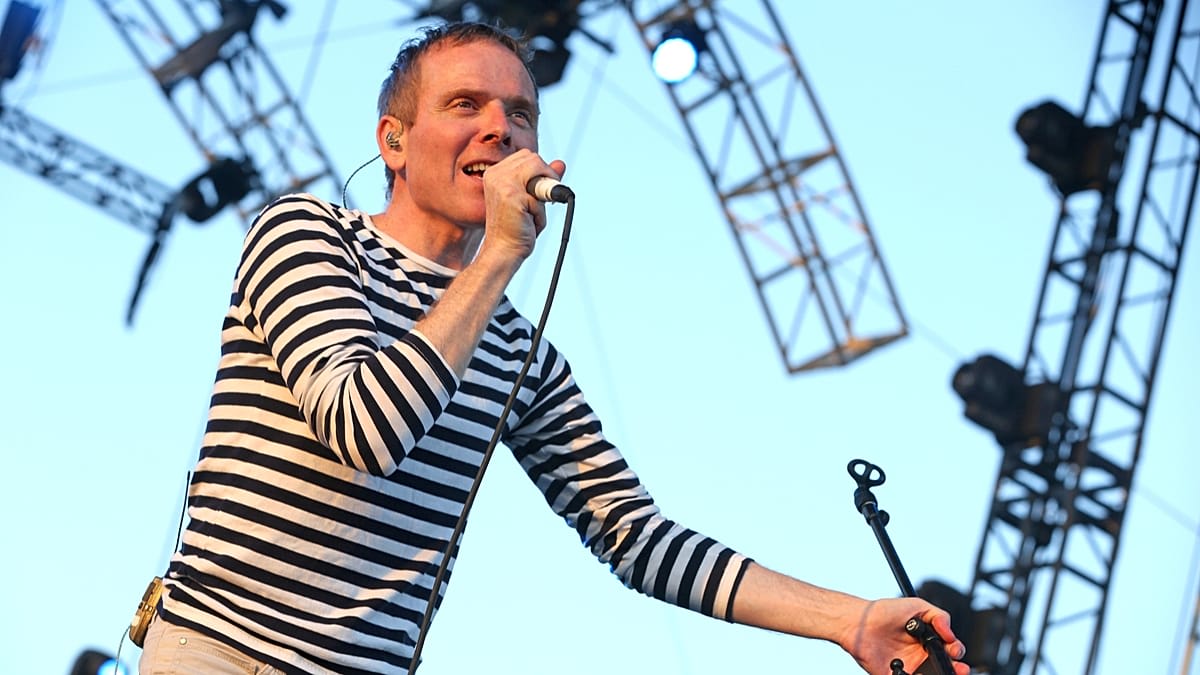 Belle and Sebastian band members performing with Scottish flag and football imagery in background