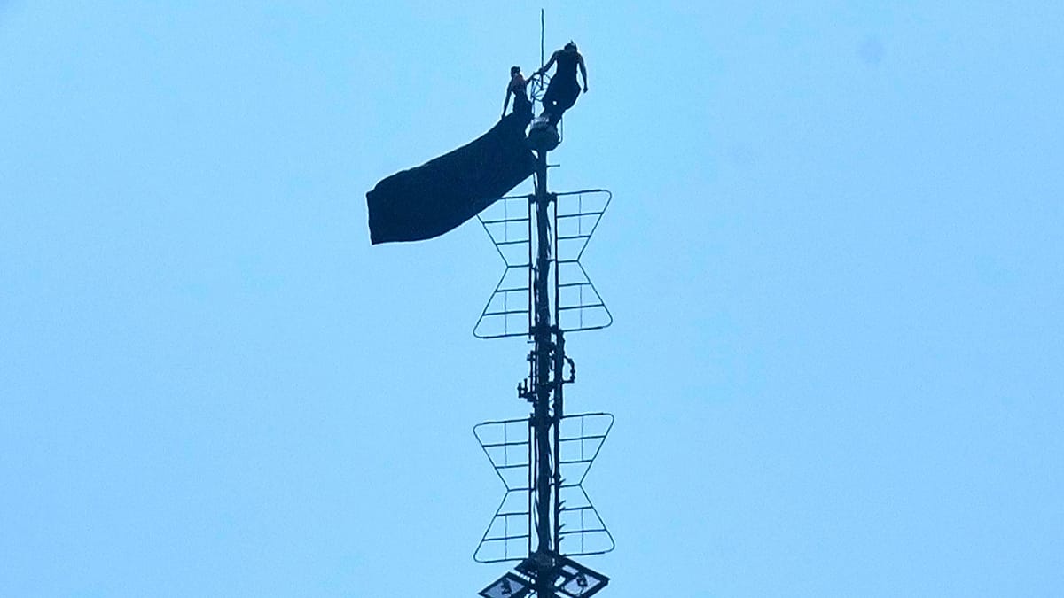 Two climbers in black clothing balanced on Empire State Building antenna holding peace banner