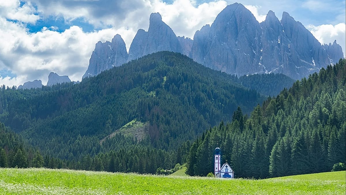** Scenic mountain hiking trail winding through European Alps with distant peaks visible